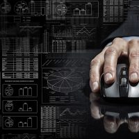 A hand on a computer mouse in front of architectural drawings